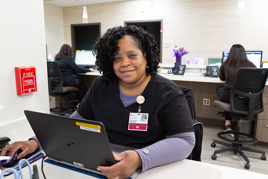 A smiling Healient healthcare provider sitting at a desk in front of a laptop
